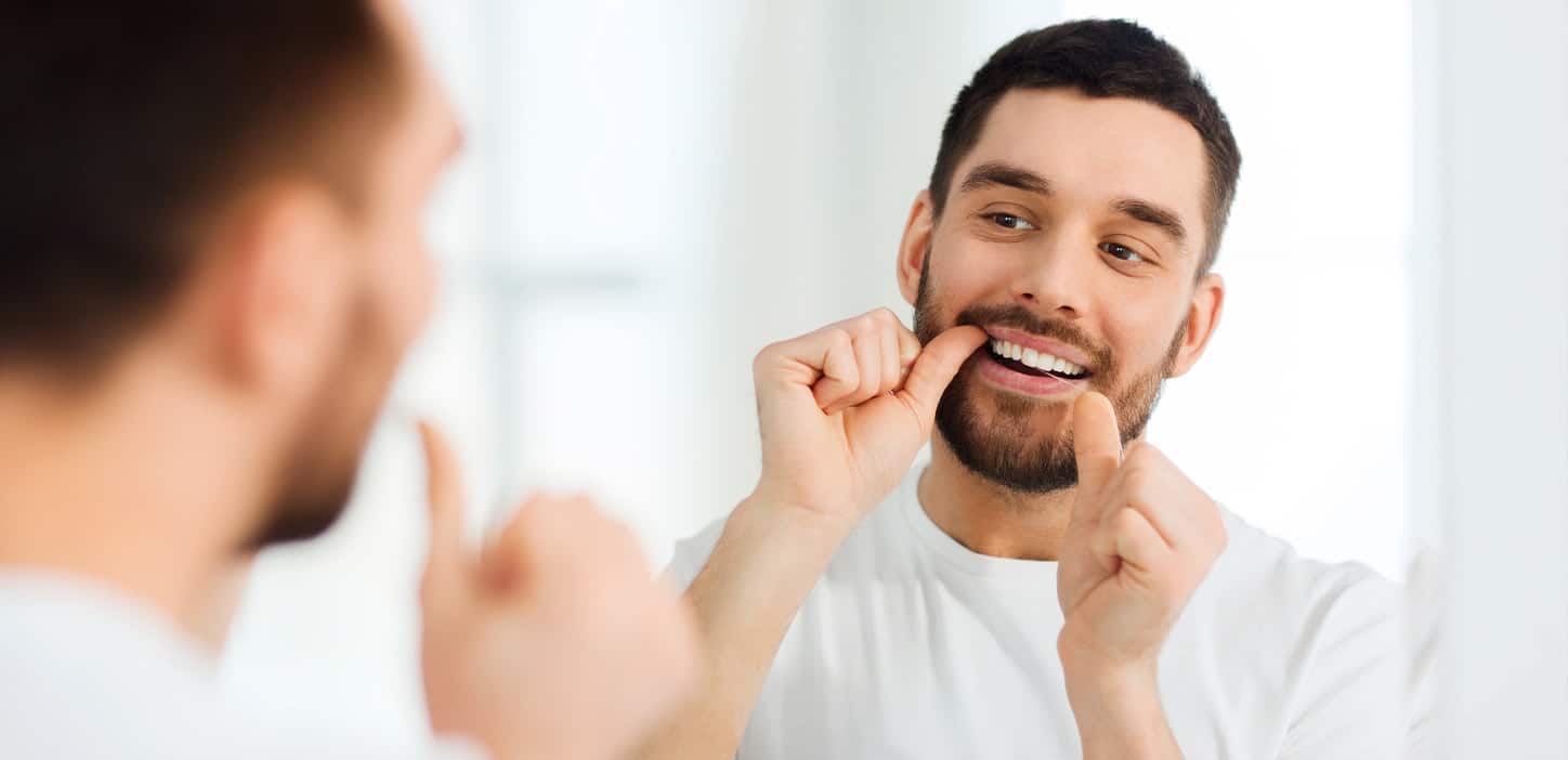 man flossing teeth in mirror