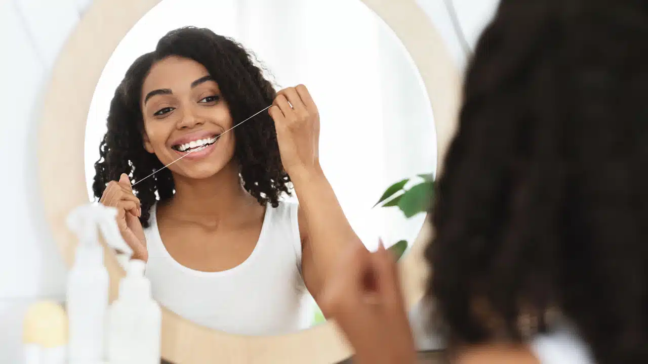 Woman flossing her teeth in mirror at home