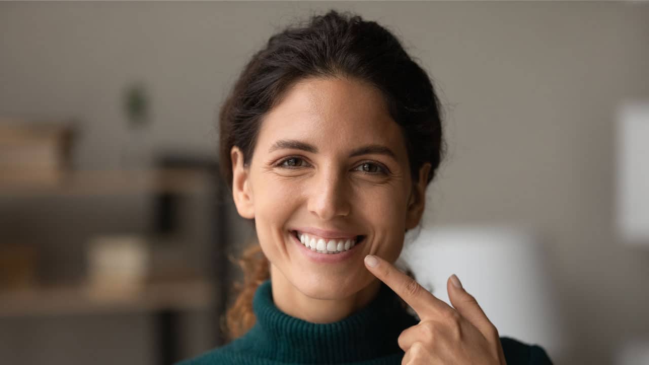 Woman with dental implants smiling and pointing at teeth